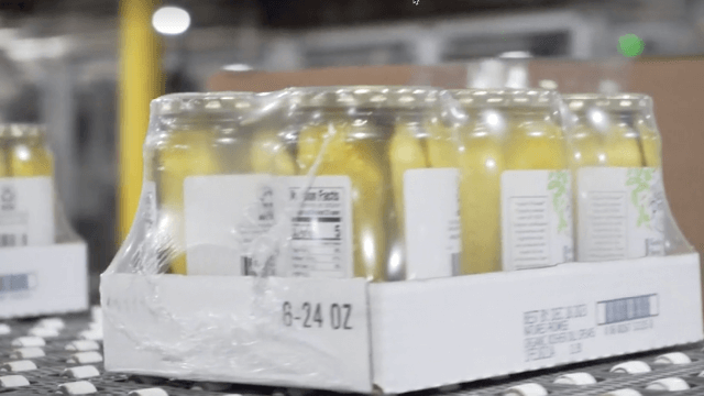 Cases of pickles move down a conveyor system as part of packaged produce solutions, adhering to produce labeling requirements. Produce labeling, packaged produce solutions, produce labeling requirements.