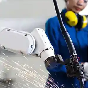 Robot welding arm in the foreground with worker in the background.