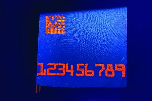 orange fluorescent numbers and QR code sample marks on a blue background. The marks are on the end of a square piece of lumber.