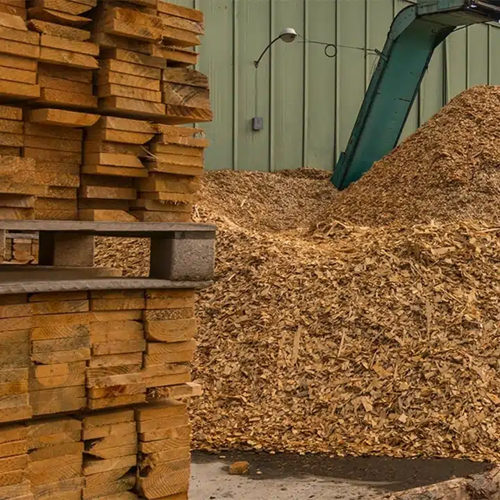Stacked lumber beside a large pile of wood chips at a sawmill.