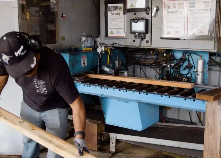 Worker handling lumber beside industrial production equipment