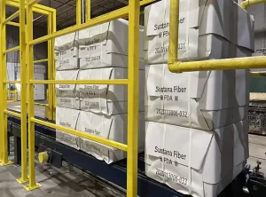 Large product cubes wrapped in white paper on a conveyor. The cubes have been marked in black ink with QR codes and alphanumeric characters.