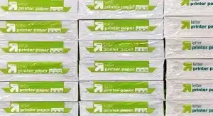 Stacks of packaged letter-size printer paper with green and white labels arranged in rows.