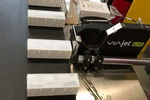 Matthews Marking Systems VIAjet L12 thermal inkjet printer marking white product cartons as they move along a production conveyor.