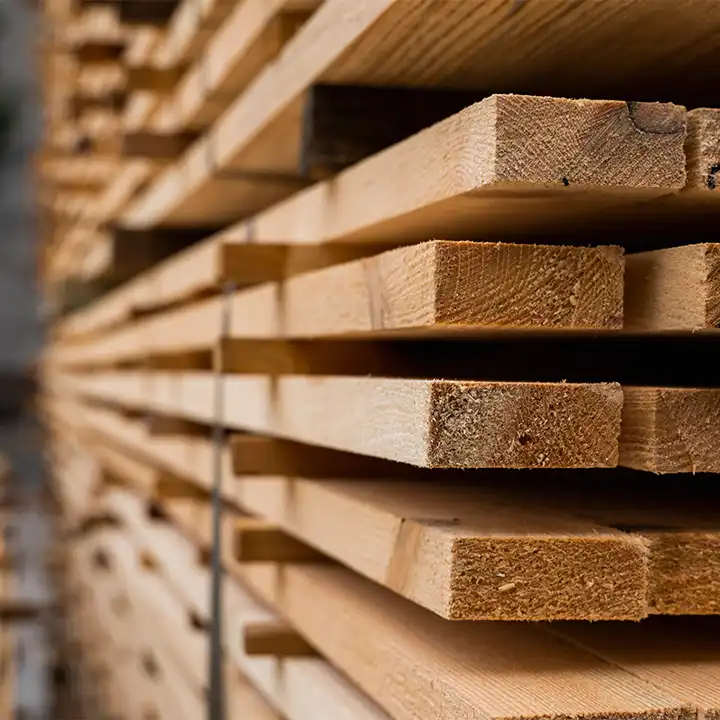 Close-up of stacked wooden lumber boards showing natural wood grain and cut edges in a lumber storage facility.